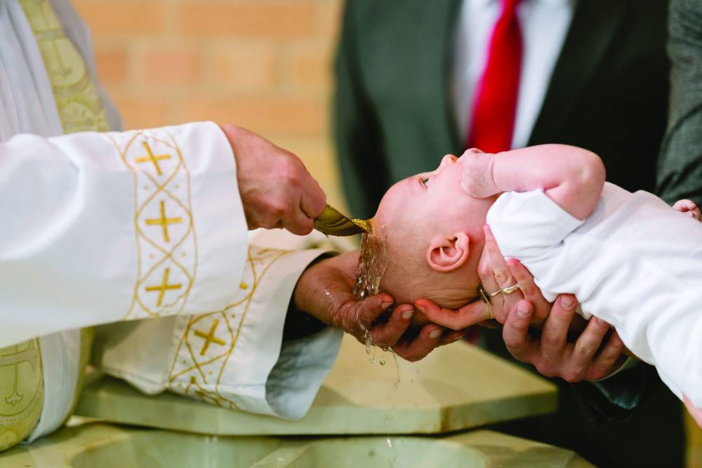 A priest is feeding a baby with a spoon.