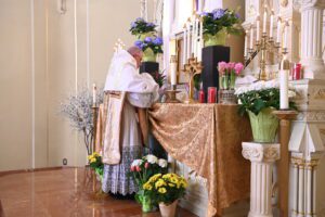 Priest conducting a ceremony at an altar adorned with flowers.