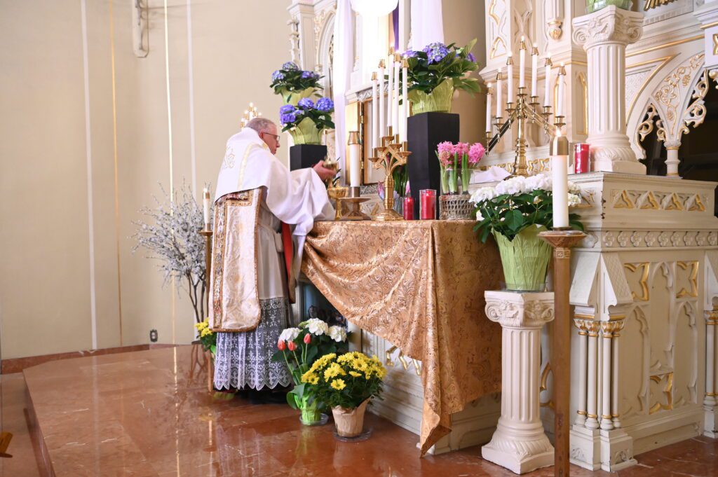Priest performing a religious ceremony at an altar adorned with flowers.